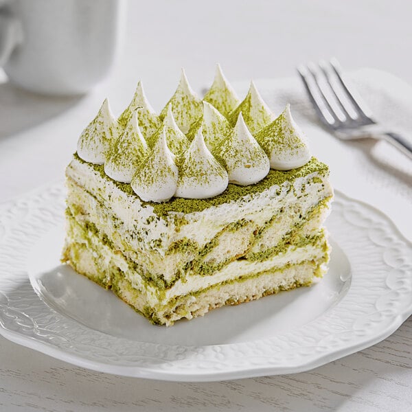A piece of cake with green frosting next to a white cup of Matcha.Com matcha powder.