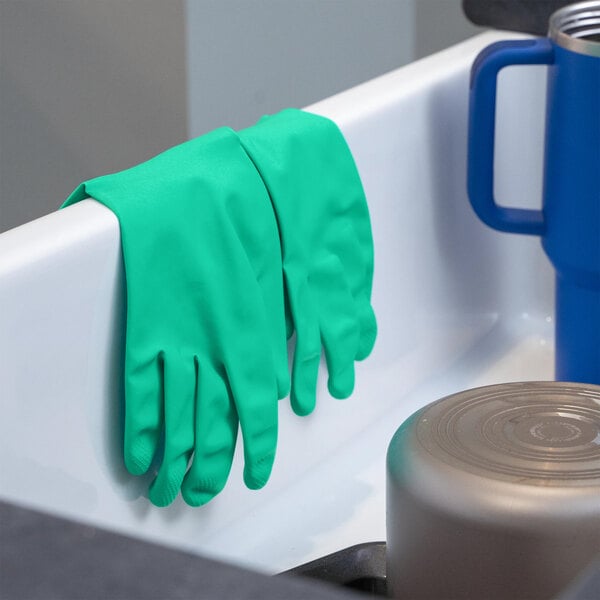 A pair of green heavy-duty unlined nitrile rubber gloves draped over the edge of a sink.