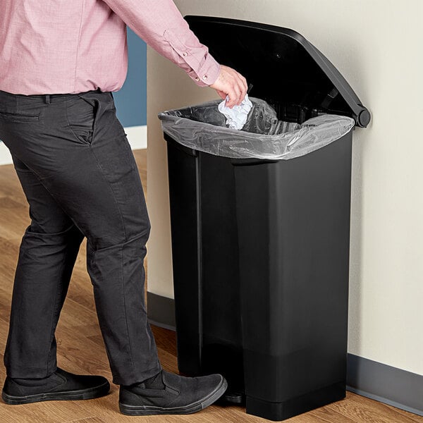 A man standing next to a Lavex rectangular black step-on trash can.