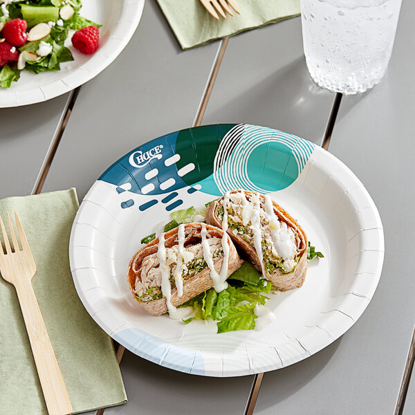 A Choice paper plate with a salad, raspberries, and almonds on a table.