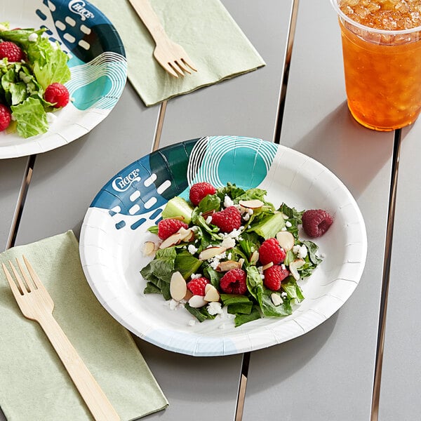 A Choice Lifestyle paper plate with salad, raspberries, and nuts on a table with a drink.