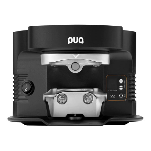 A black and silver PUQpress M5 automatic espresso tamper on a table next to a black and silver coffee machine.