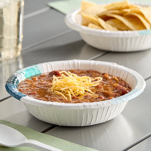 A white paper bowl of chili with chips and a spoon in it.