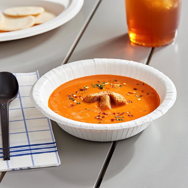 A white heavy weight paper bowl filled with soup on a table.