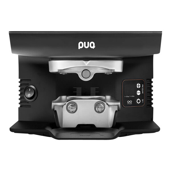 A black PUQpress M6 automatic espresso tamper on a table with a pou coffee machine.