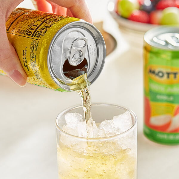 A hand pouring Mott's Apple Juice from a yellow can into a glass of ice.