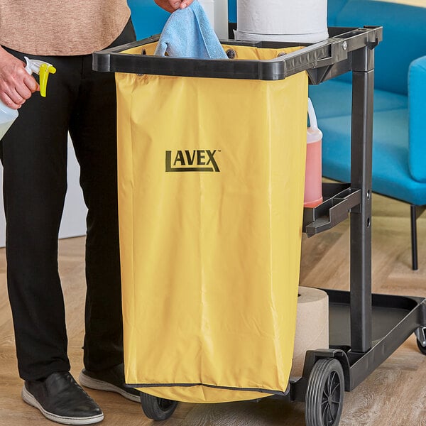 A man using a yellow Lavex janitor cart bag to clean a kitchen.