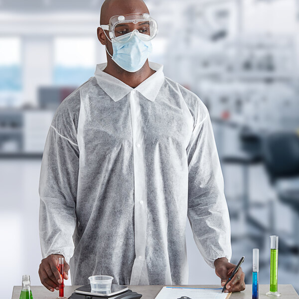 A man wearing a Cordova white economy weight polypropylene lab coat and face mask holding a test tube.