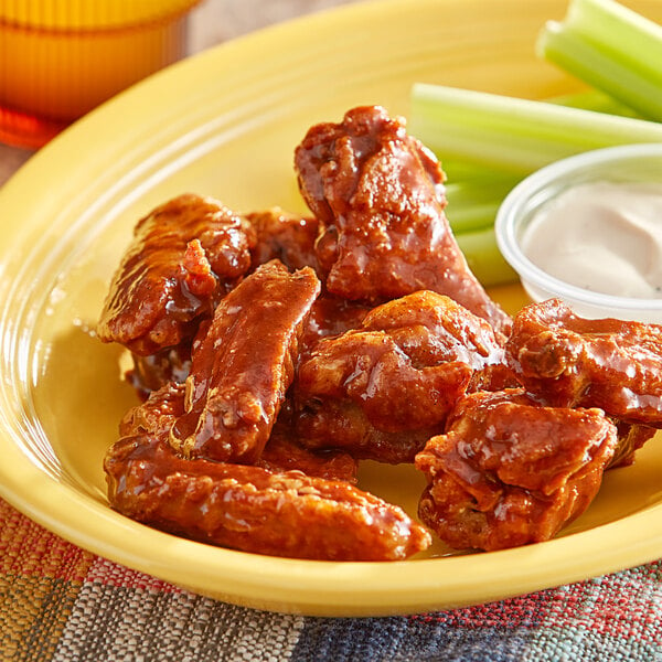 A plate of chicken wings with celery sticks and Tajin Mild Hot Sauce.