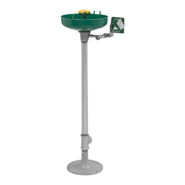 A green and white pedestal-mounted Haws eye and face wash station with a black and silver device on top.