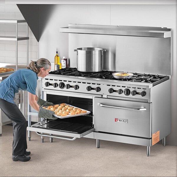 A woman putting a tray of food in a large Wolf stainless steel oven.