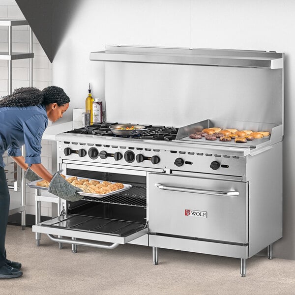 A woman putting food in a Wolf commercial gas oven.