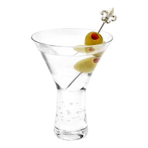 A martini glass with a stainless steel cocktail pick topped with a fleur de lis holding olives.