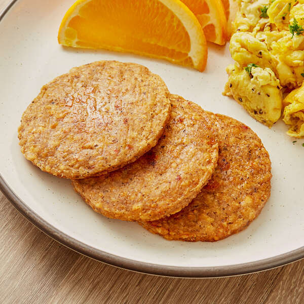 Two Tindle plant-based breakfast sausage patties on a plate with an orange slice.