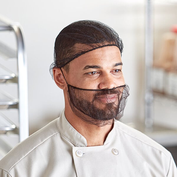 A man in a chef's uniform wearing a black nylon hairnet over his head.