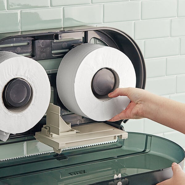 A hand touching a Lavex Universal Jumbo toilet paper roll.