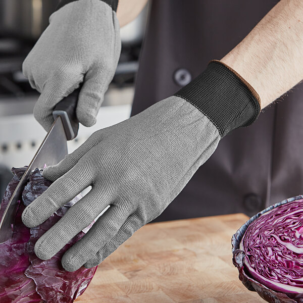 The hand of a person wearing an Armor Guys Kyorene Pro cut-resistant glove cutting a red cabbage on a wooden surface.