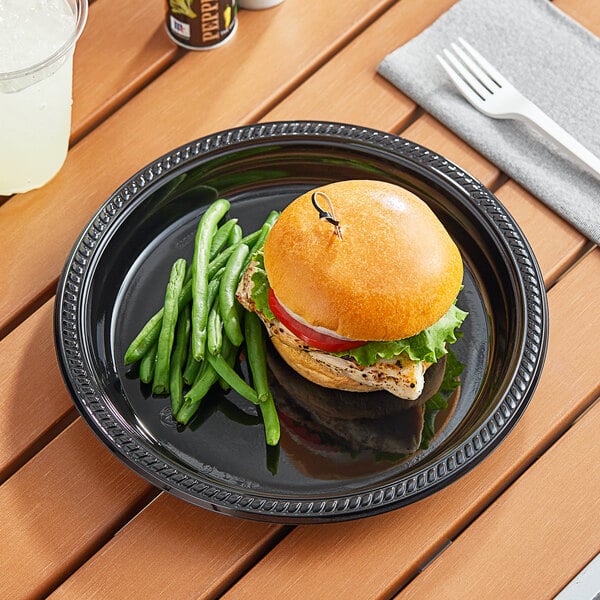 A Choice black plastic plate with a burger and green beans on a table.