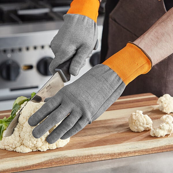 A person wearing Armor Guys Kyorene Pro cut-resistant gloves cutting cauliflower on a cutting board.