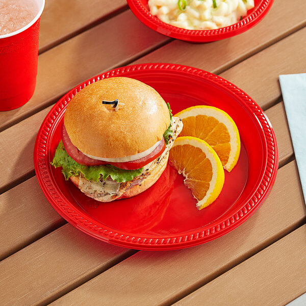 A burger and orange slices on a Choice red plastic plate.