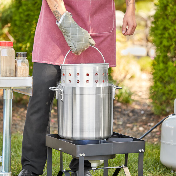 A man in a chef's apron using a Choice aluminum stock pot to cook on a grill.