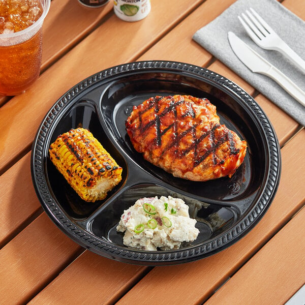 A Choice black plastic plate with food including chicken and corn on a table.