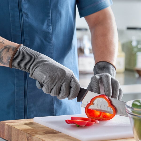 A pair of gray cut-resistant food-safe gloves being worn while slicing a red bell pepper on a cutting board.