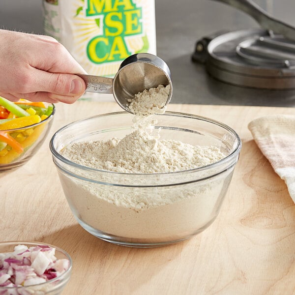 A person pouring Maseca corn flour into a bowl.