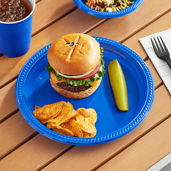 A Choice blue plastic plate with a hamburger and chips on a table.