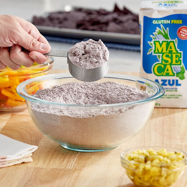 A hand holding Maseca Blue Corn Masa Flour over a bowl.