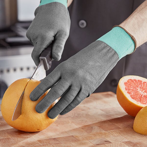 A person's hand in an Armor Guys Kyorene Pro glove using a knife to cut an orange.