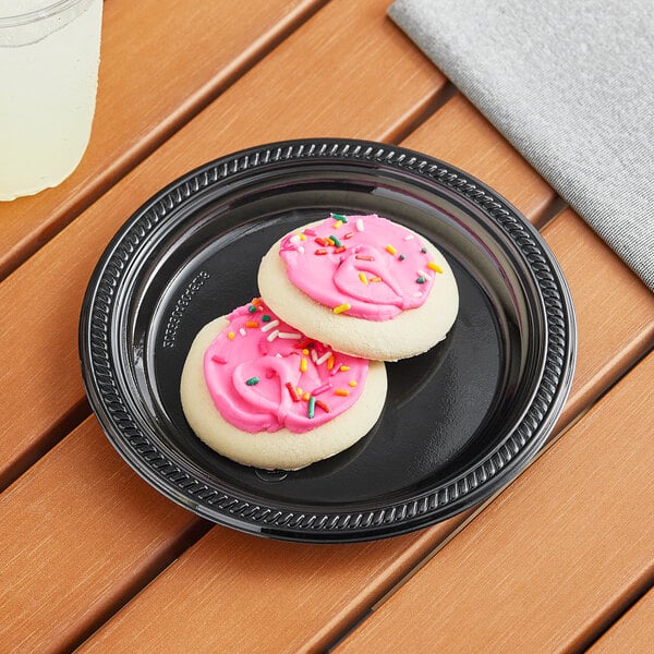 Two Choice black plastic plates with cookies with pink frosting and sprinkles on them.