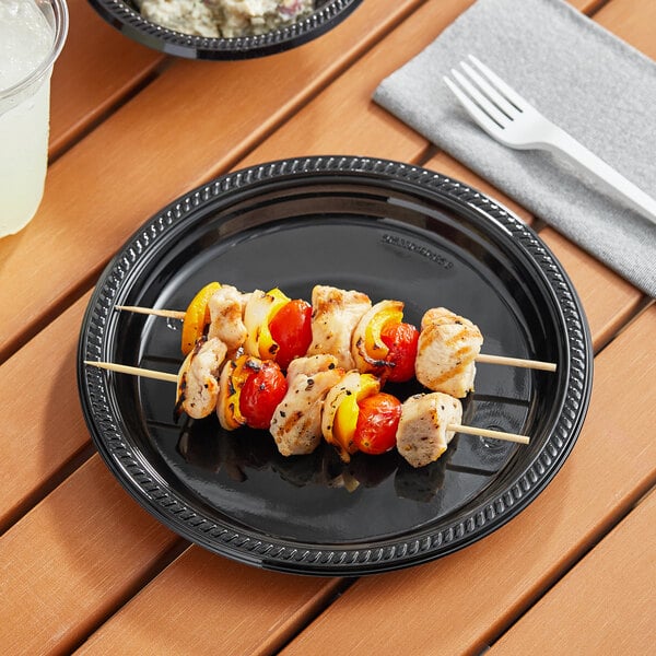 A Choice black plastic plate with chicken skewers and vegetables on a table.