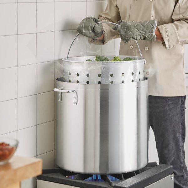 A man using a Choice aluminum stock pot to cook broccoli.