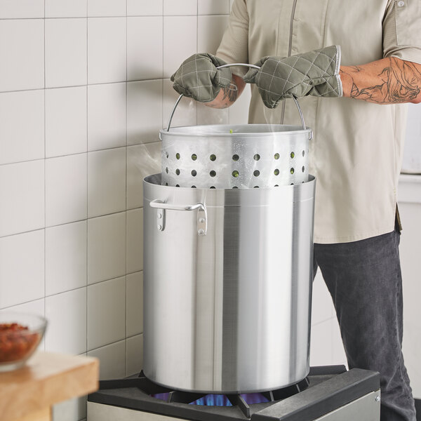 A person in an apron and gloves holding a Choice large aluminum stock pot.