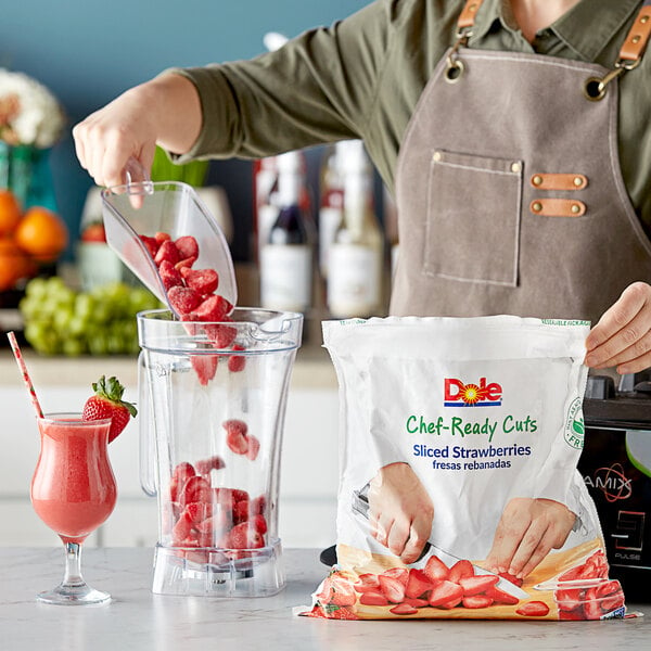 A woman pouring Dole Chef-Ready Cuts IQF Sliced Strawberries into a blender on a counter.