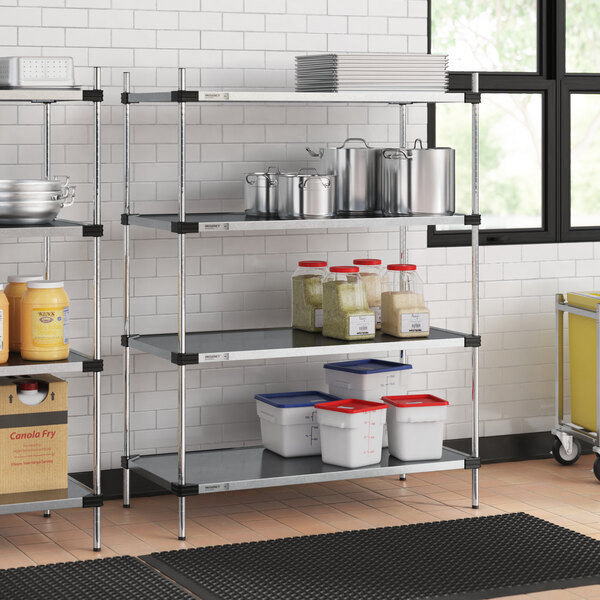 A Regency galvanized steel shelving unit in a professional kitchen with white and blue plastic containers on the shelves.