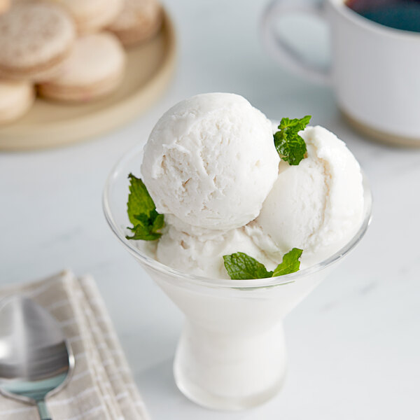 A glass bowl of Pitaya Foods Organic Coconut Sorbet with mint leaves.