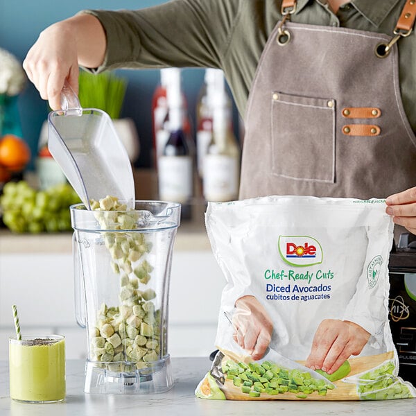 A person pouring Dole Chef-Ready Cuts IQF diced avocado into a blender on a table.
