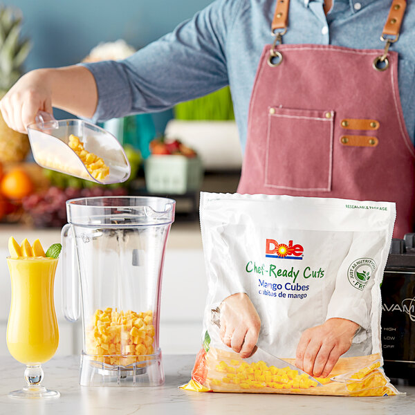 A person pouring Dole Chef-Ready Cuts IQF Cubed Mango into a blender.