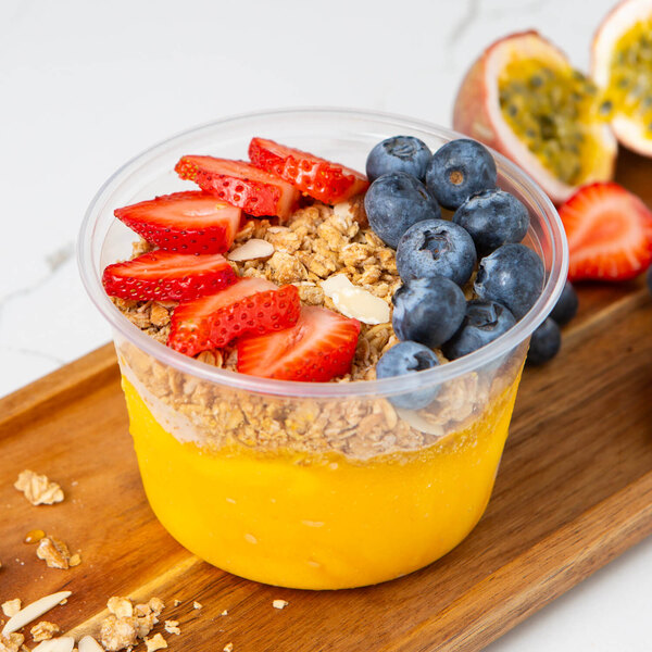 A bowl of Pitaya Foods organic passion fruit sorbet with granola and berries on a table in a juice bar.