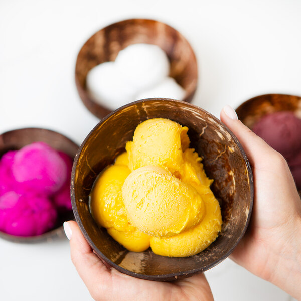 A hand holding a bowl of yellow Pitaya Foods Organic Passion Fruit Sorbet.
