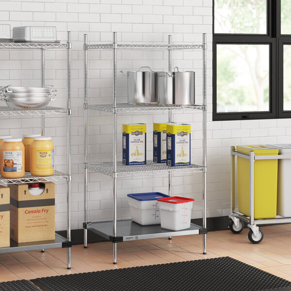 A metal Regency wire shelving unit with a solid metal bottom shelf holding plastic containers with blue lids.