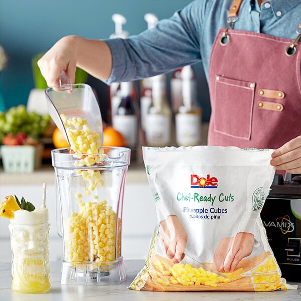 A person pouring Dole Chef-Ready Cuts IQF Cubed Pineapple into a blender.