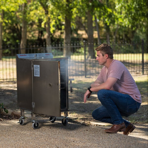 A man kneeling next to a SmokinTex electric smoker box with the door open.
