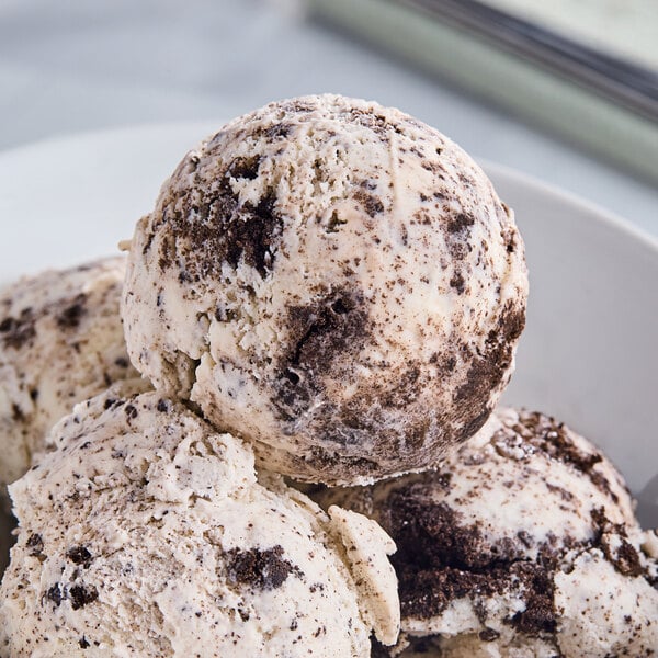 A bowl of Tillamook Cookies and Cream ice cream with a scoop of white ice cream with brown cookie pieces.