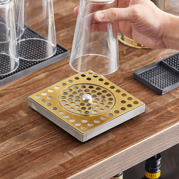 A hand holding a glass over a Regency gold surface-mount beer drip tray.