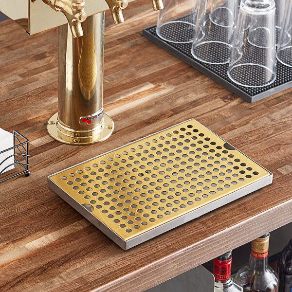 A Regency PVD gold metal plate with holes on a bar counter with beer glasses.