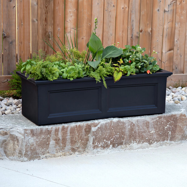 A black Mayne Fairfield garden bed planter with various plants in it.