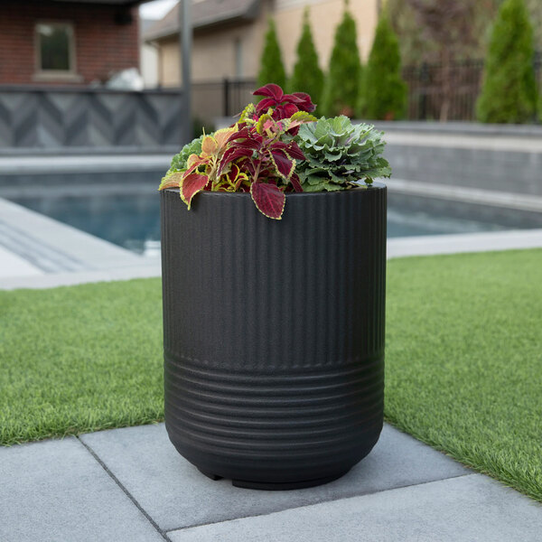 A black Mayne Arden round planter with plants in it on a grassy area.